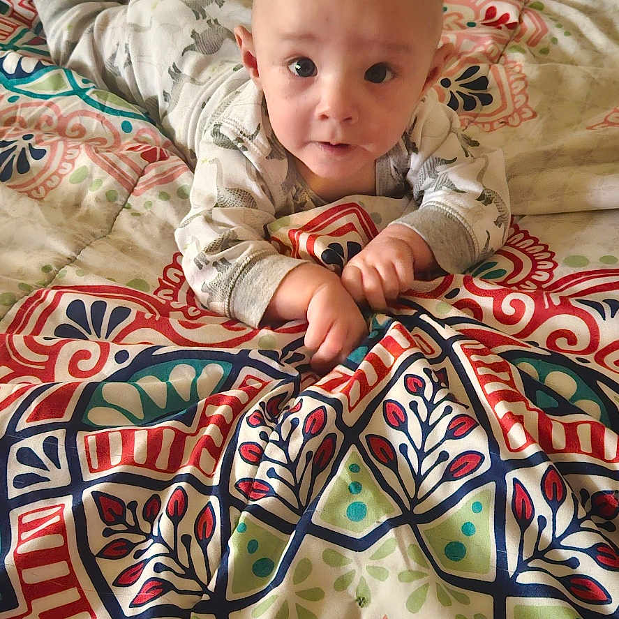 Jordan Jr joined the competition — help win amazing prizes! baby, bedroom, blanket, child, clothing, cozy, curious, drawer, eyes, face, furniture, hands, head, indoor, infant, long_sleeve, lying_down, patterned_blanket, plastic_storage, soft_toys