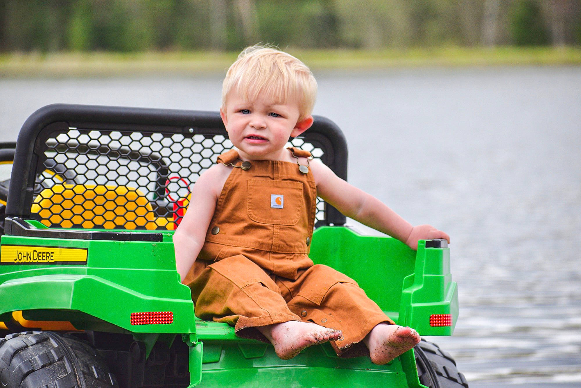 Brantley is registered to the contest to win money with this photo: automotive_design, automotive_exterior, automotive_tire, automotive_wheel_system, baby_toddler_clothing, child, fun, grass, lake, leisure, motor_vehicle, person, recreation, riding_toy, sorrow, tire, toddler, toy, vehicle, water