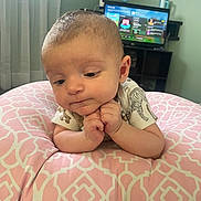 Elias is registered to the contest to win money with this photo: baby, infant, cushion, pink, pattern, hands, face, expression, indoor, room, television, screen, game, clothing, short_sleeve, curtain, window, furniture, person, child