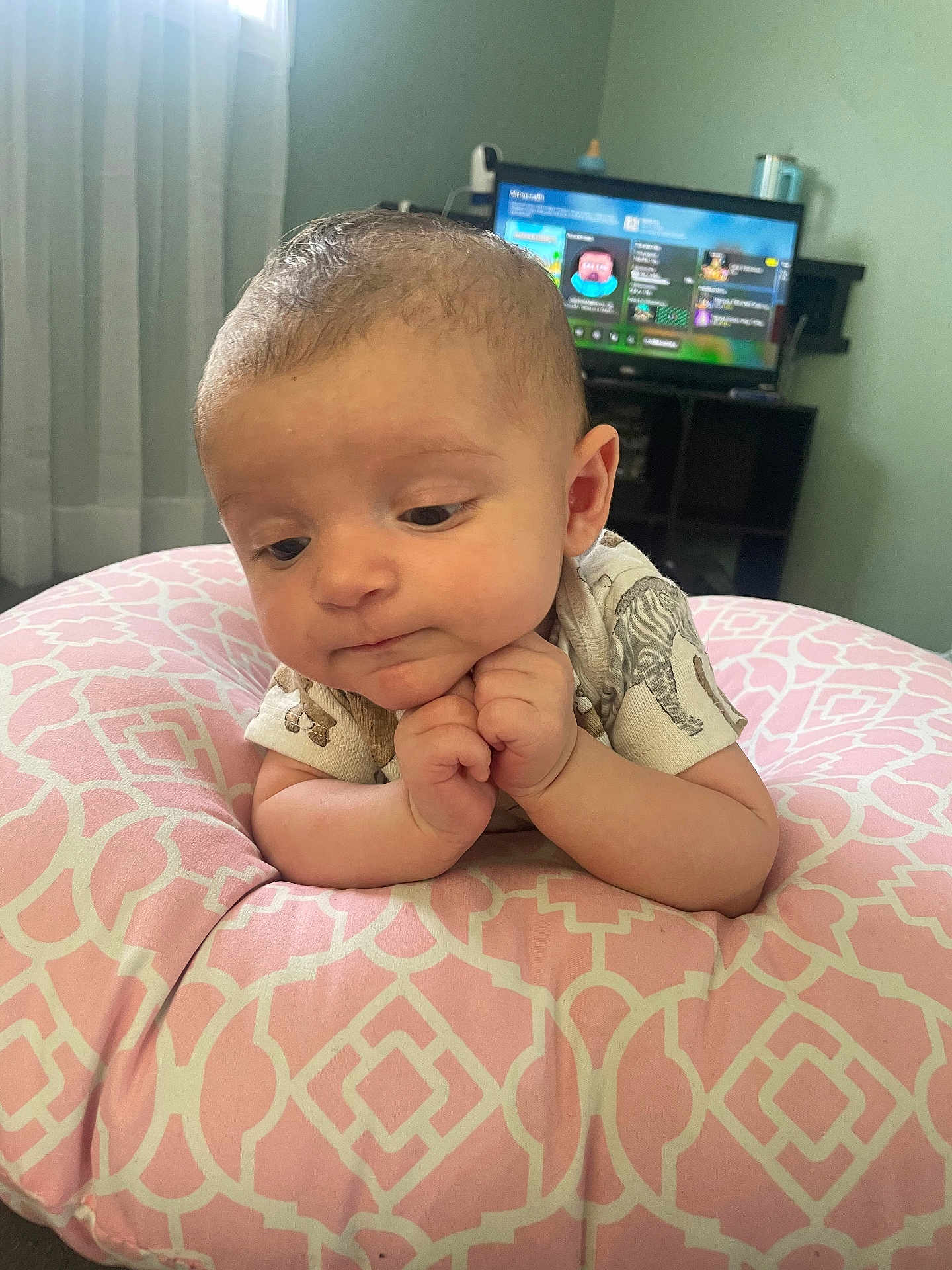Elias is registered to the contest to win money with this photo: baby, infant, cushion, pink, pattern, hands, face, expression, indoor, room, television, screen, game, clothing, short_sleeve, curtain, window, furniture, person, child
