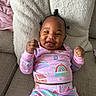 Amora is registered to the contest to win money with this photo: baby, child, smiling, pajamas, rainbow, gingerbread_house, fist, couch, pillow, plush, cozy, happy, indoor, person, infant, cute, clothing, relaxing, portrait, skin