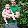 adult, child, toddler, person, smile, greenery, forest, outdoor, nature, holding, happy, casual_clothing, shorts, tshirt, pigtails, grass, trees, daylight, family, portrait