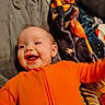 Emma is registered to the contest to win money with this photo: baby, infant, orange_clothing, smiling, happy, blanket, fabric, soft, lying_down, child, face, cute, warm, cozy, indoors, colorful, playful, person, head, expression