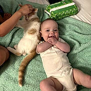Emma is registered to the contest to win money with this photo: baby, cat, child_hand, green_towel, bed, petting, happy, smiling, infant, animal, domestic_cat, white_clothing, relaxed, cute, indoor, person, furniture, playful, friendship, cozy