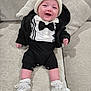 baby, infant, child, smiling, tuxedo_onesie, bow_tie, beanie, jacket, socks, booties, couch, cushion, sitting, indoor, portrait, cute, happy, soft_fabric, relaxed, hands