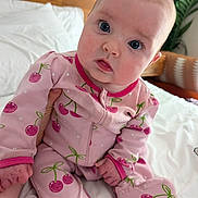 Evelyn is registered to the contest to win money with this photo: baby, infant, pink_onesie, cherry_pattern, bed, bedding, wooden_headboard, plant, indoors, child, cute, portrait, person, sitting, face, hand, footed_pajamas, expression, curious, cozy