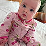 baby, infant, pink_onesie, cherry_pattern, bed, bedding, wooden_headboard, plant, indoors, child, cute, portrait, person, sitting, face, hand, footed_pajamas, expression, curious, cozy
