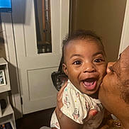 Kalilah is registered to the contest to win money with this photo: baby, infant, child, smile, laugh, kiss, adult, person, face, eyes, onesie, hand, affection, joy, home_interior, door, mirror, shelf, television, furniture