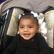 Lilly joined the competition — help win amazing prizes! child, toddler, smiling, car_seat, blanket, white_bows, hair_accessory, clothing, black_sweater, face, happy, baby, indoor, portrait, seatbelt, infant, cute, young_child, baby_girl, cozy