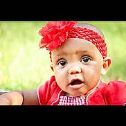 Dorothy is registered to the contest to win money with this photo: baby, child, closeup, curious, cute, expression, eyes, face, fashion_accessory, flower, green_background, headband, infant, natural_light, outdoor, portrait, red_clothing, skin, summer, young_child