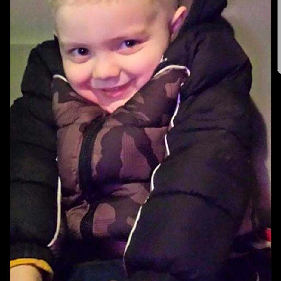 Dom is registered to the contest to win money with this photo: child, boy, jacket, puffy_jacket, smile, face, hands, sitting, indoor, casual_clothing, young, cute, portrait, hairstyle, playful, person, fun, warm_clothing, expression, cozy