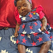 Janiyah is registered to the contest to win money with this photo: baby, infant, child, sleepy, blue_dress, red_shirt, headband, bed, blanket, patterned_clothing, stars, indoors, skin, legs, feet, hand, cute, resting, portrait, person