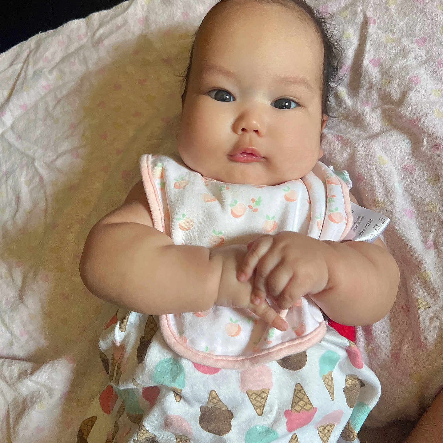 Rhianna joined the competition — help win amazing prizes! adorable, baby, bib, blanket, child, clothing, cute, expression, face, hands, ice_cream_pattern, indoors, infant, lying_down, orange_bow, person, portrait, skin, soft_texture, young