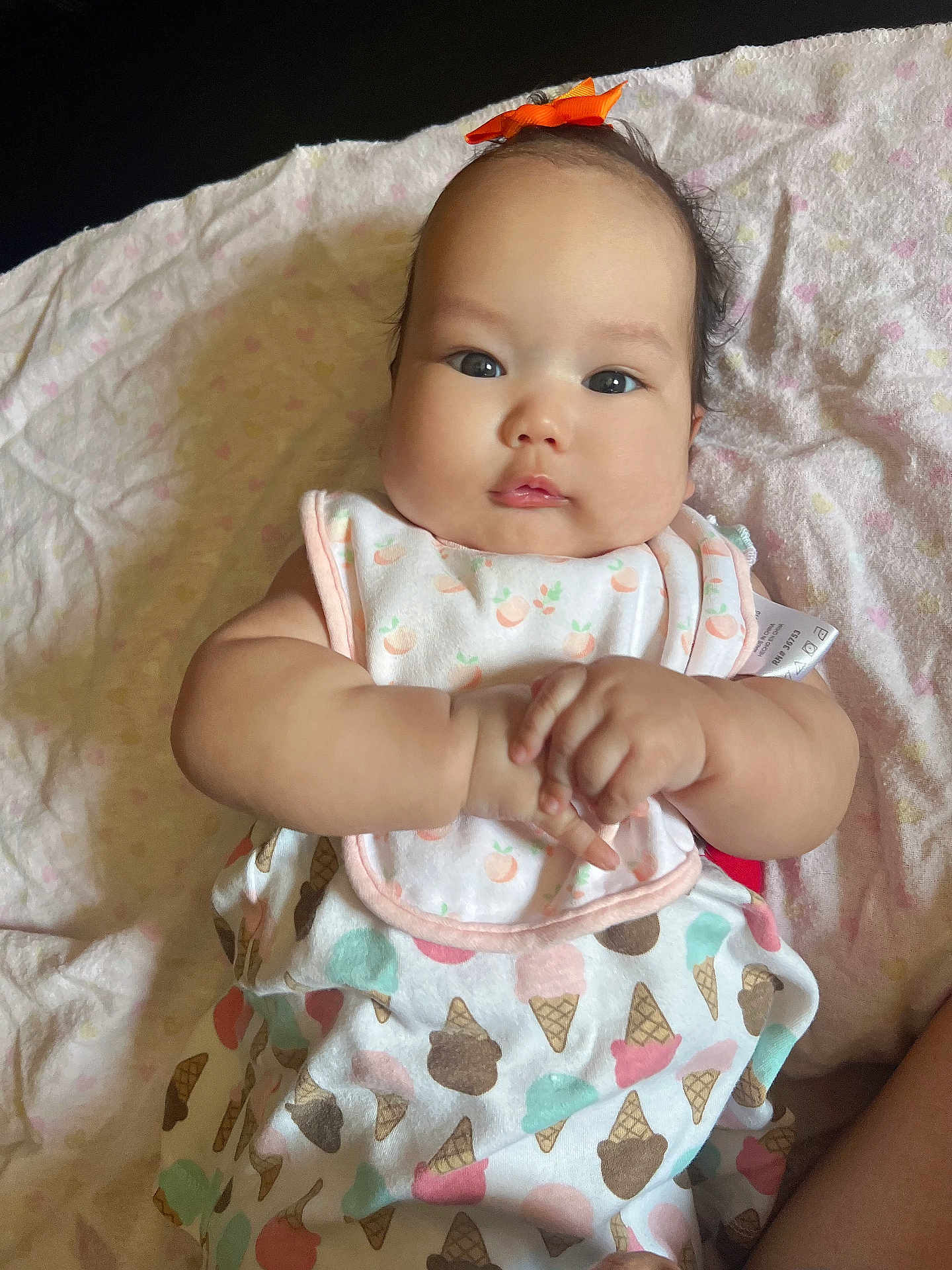 Rhianna joined the competition — help win amazing prizes! baby, infant, child, bib, orange_bow, blanket, clothing, ice_cream_pattern, cute, hands, face, portrait, soft_texture, lying_down, indoors, skin, expression, adorable, young, person