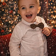 Sohan participe au concours pour gagner de l'argent avec cette photo : toddler, child, boy, smiling, happy, white_shirt, bow_tie, holiday, festive, bokeh, lights, snow, portrait, indoors, warm_lighting, cute, cheerful, celebration, red_chair, casual_clothing