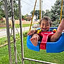 toddler, swing, baby_swing, child, smiling, happy, outdoor, grass, fence, porch, foot, playful, daytime, tree, house, baby, person, seat, metal_rail, curly_hair