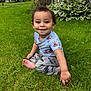 toddler, child, grass, outdoor, smiling, blue_shirt, pants, barefoot, garden, plants, wooden_fence, greenery, happy, sitting, casual_clothing, daylight, portrait, playful, cute, nature