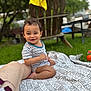 toddler, child, outdoor, grass, blanket, striped_shirt, diaper, smiling, person, wooden_chair, yellow_cloth, leg, nature, greenery, playtime, happy, summer, park, casual, daytime