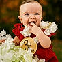 baby, child, smiling, red_dress, white_flowers, portrait, cute, happy, outdoor, nature, infant, flower_garland, close_up, young, skin, face, eyes, hand, laughing, background_blur