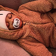Josiah is registered to the contest to win money with this photo: baby, sleeping, pacifier, hat, onesie, fuzzy_clothing, infant, child, face, cozy, warm, resting, portrait, indoor, cute, peaceful, soft_texture, headwear, zipped_jacket, relaxation