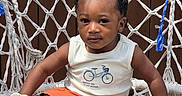 Josiah is registered to the contest to win money with this photo: braided_hair, brown_background, casual, child, cute, daytime, expression, footwear, hammock_chair, orange_shorts, outdoor, person, sitting, sneakers, summer_clothing, sunlight, toddler, white_shirt, woven_chair, young_child
