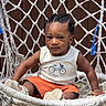 Josiah is registered to the contest to win money with this photo: toddler, child, braided_hair, white_shirt, orange_shorts, sneakers, hammock_chair, woven_chair, outdoor, sunlight, brown_background, cute, sitting, expression, person, summer_clothing, young_child, footwear, casual, daytime