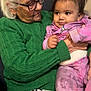 elderly_woman, baby, glasses, green_sweater, pink_outfit, indoor, seated, leopard_print, holding, affection, family, person, portrait, caring, happy, child, senior, cute, warmth, love