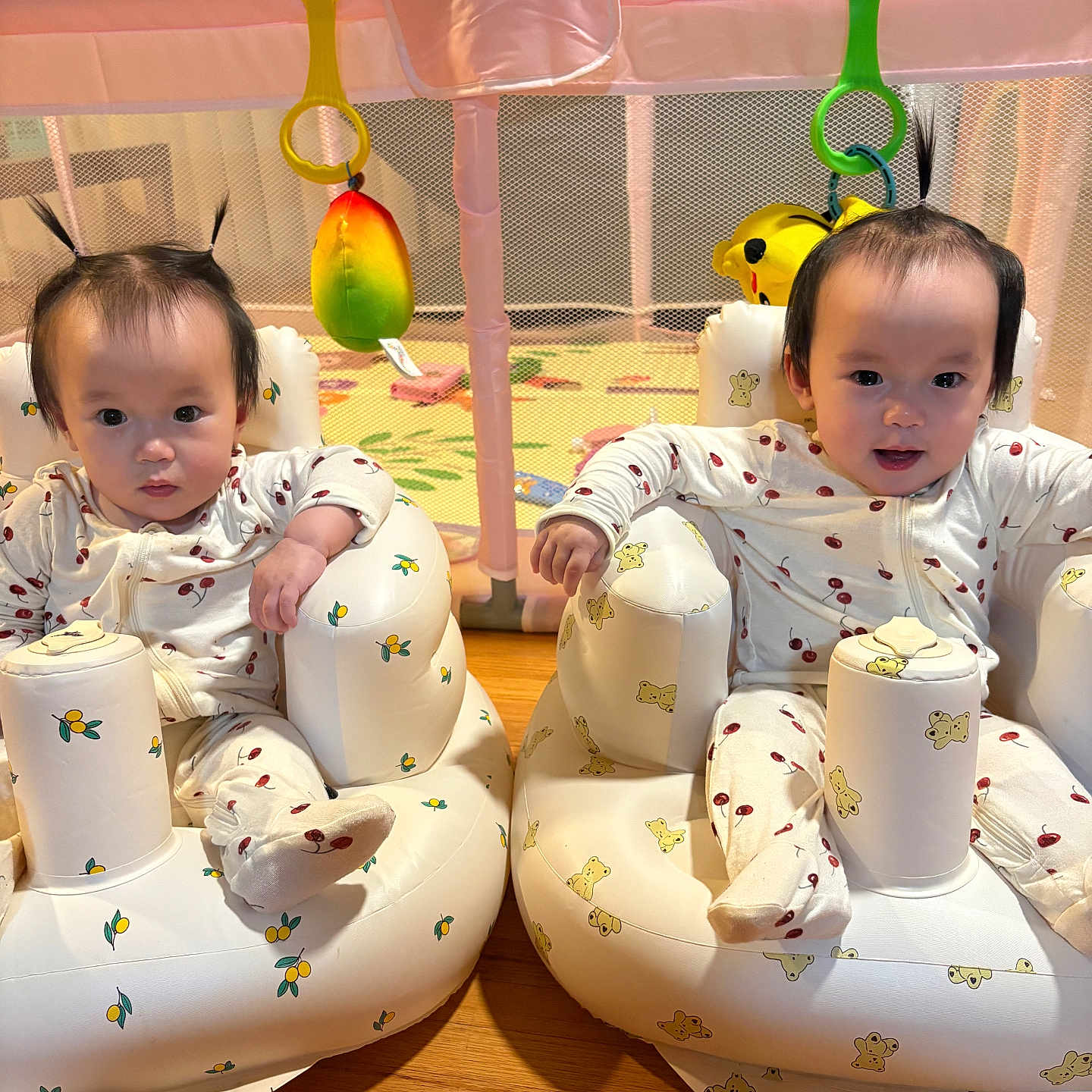 Anna And Hanna is registered to the contest to win money with this photo: baby, child, colorful, cute, face, floor, hair_ponytail, indoor, infant, inflatable_seat, matching_clothes, pajamas, person, playful, playpen, sitting, smile, toddler, toy, wooden_floor