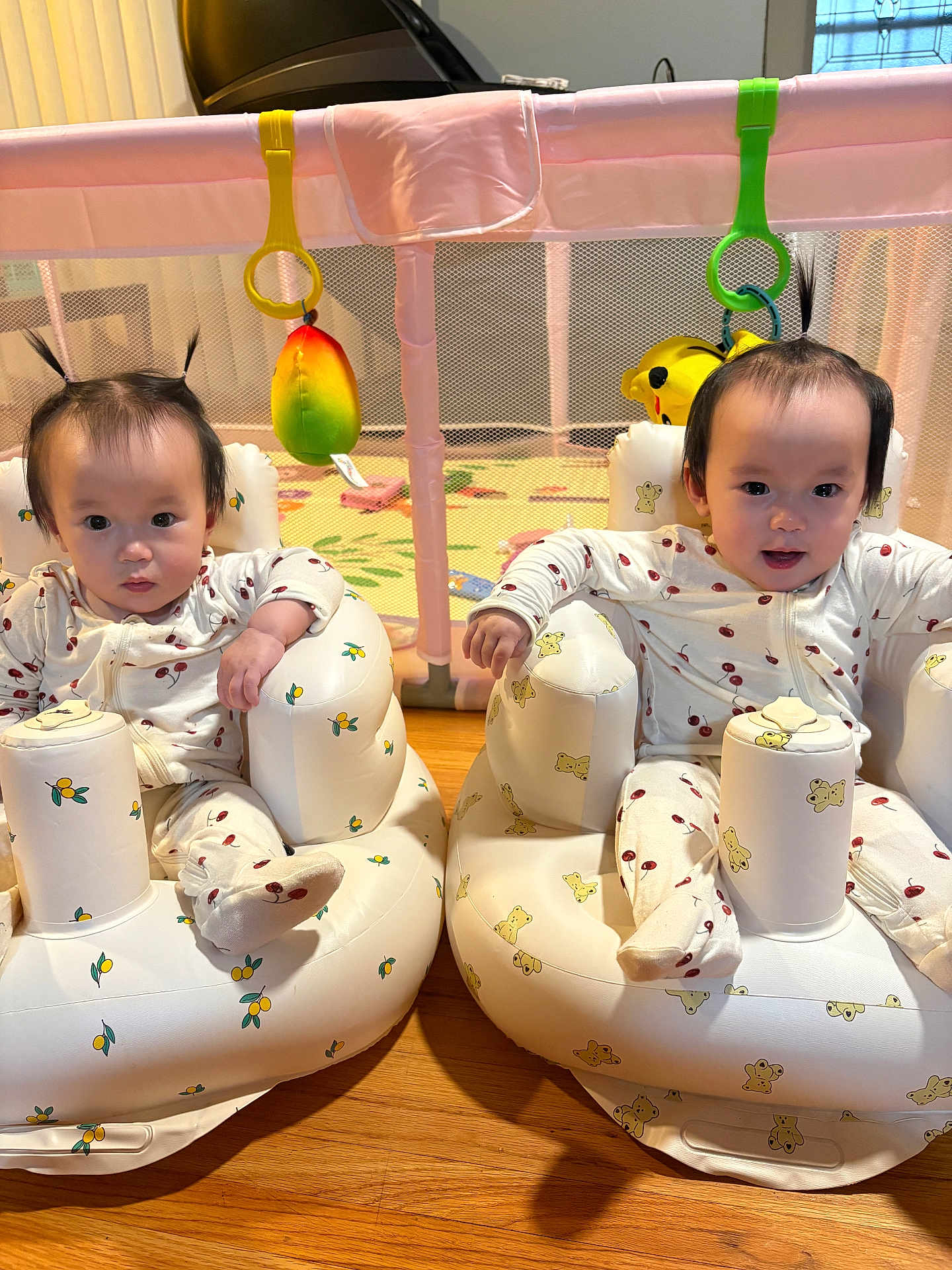 Anna And Hanna is registered to the contest to win money with this photo: baby, infant, child, playpen, inflatable_seat, pajamas, floor, toy, hair_ponytail, matching_clothes, indoor, cute, playful, sitting, face, person, wooden_floor, colorful, smile, toddler