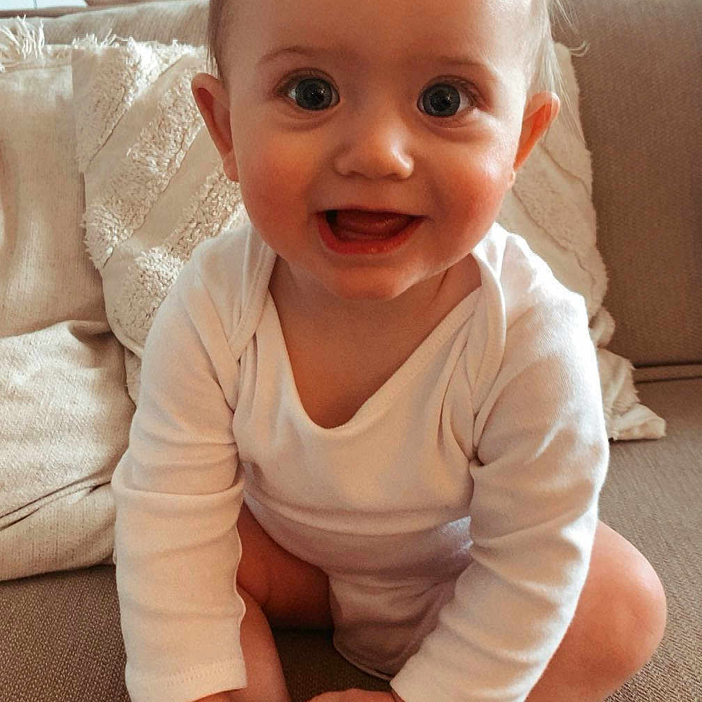 Ama participe au concours pour gagner de l'argent avec cette photo : baby, child, couch, cute, face, feet, furniture, hands, happy, home, indoors, infant, living_room, person, portrait, sitting, skin, smiling, white_clothing, young