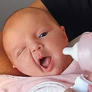 Elina participe au concours pour gagner de l'argent avec cette photo : baby, infant, bottle, feeding, pink_bib, hand, arm, skin, face, mouth, tongue, winking, person, closeup, cute, expression, holding, clothing, nurturing, care