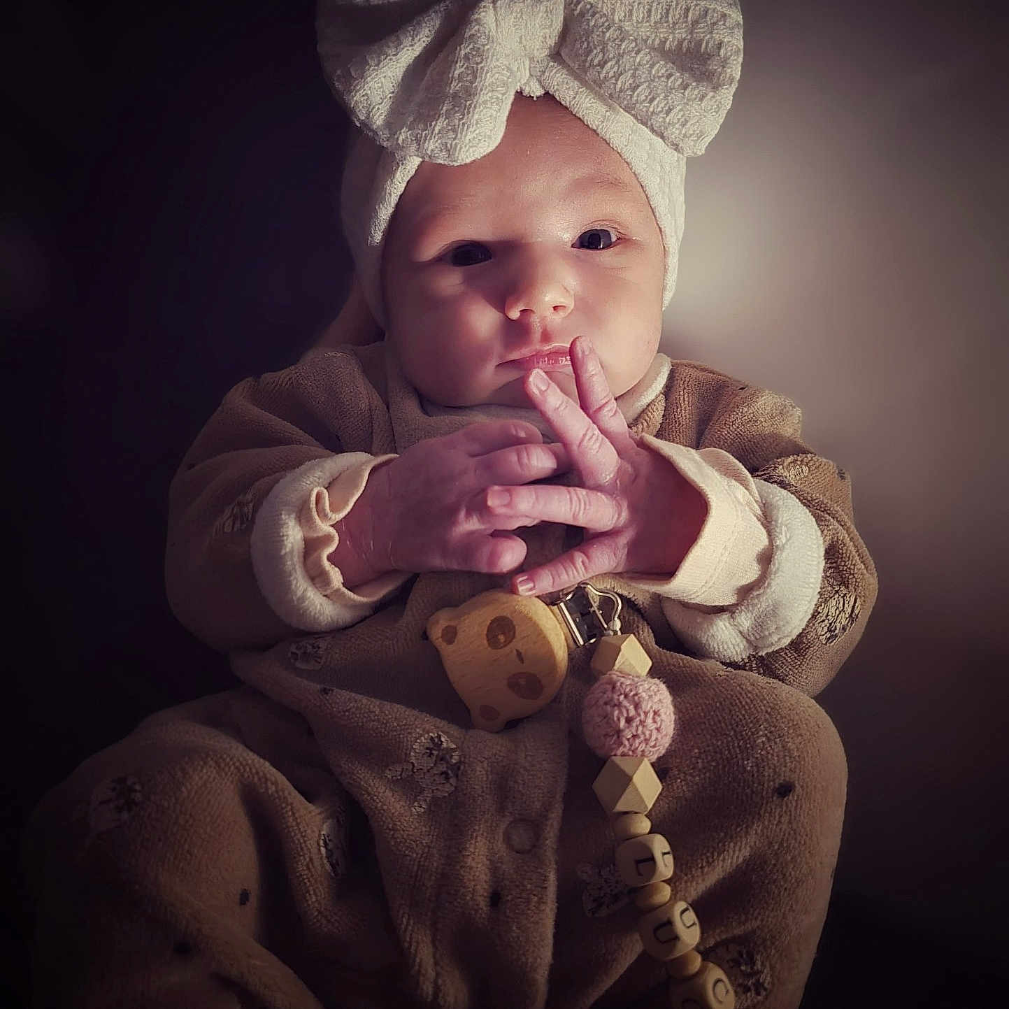 Lùcìa participe au concours pour gagner de l'argent avec cette photo : baby, child, infant, headband, bow, pajamas, clothing, hands, face, portrait, cute, soft_lighting, indoors, sitting, peaceful, newborn, accessory, wooden_toy, warm_colors, expression