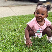 Willow is registered to the contest to win money with this photo: baby, background, car_tire, child, curly_hair, cute, daylight, grass, happy, nature, outdoor, pavement, person, pink_shirt, playful, shoes, smiling, socks, squatting, toddler