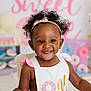 background, birthday, celebration, chair, child, colorful, curly_hair, cute, decorations, donuts, earrings, happy, headband, indoor, party, pink, portrait, smile, toddler, white_outfit