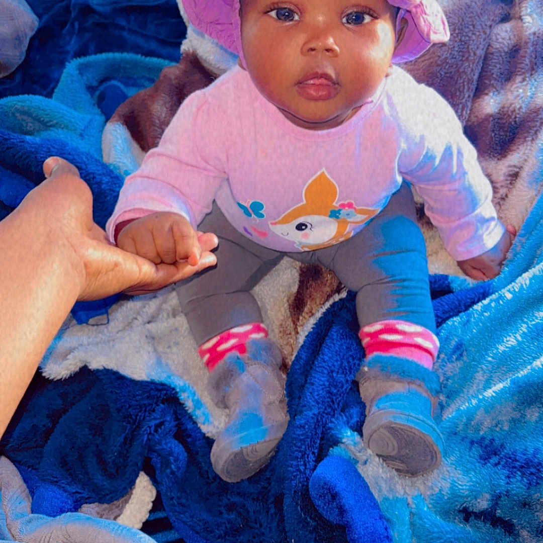 Alohianiey joined the competition — help win amazing prizes! baby, child, hat, hand, blanket, clothing, sitting, indoor, person, footwear, sock, colorful, curious, support, young_child, portrait, cute, holding_hand, soft_texture, warm