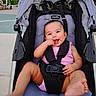 baby, child, stroller, playground, outdoor, smiling, happy, sitting, infant, pink_clothing, harness, carriage, park, play_area, barefoot, portrait, face, playful, sunlight, photograph