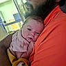 baby, infant, adult, shoulder, hug, closeup, indoor, person, face, curly_hair, orange_shirt, soft_clothing, skin, head, hand, comfort, resting, human, portrait, warm_colors