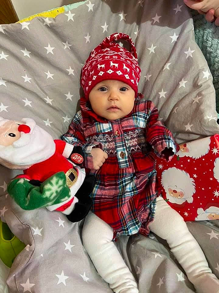 Melania is registered to the contest to win money with this photo: baby, baby_toddler_clothing, cap, christmas, christmas_decoration, christmas_eve, christmas_ornament, facial_expression, headwear, holiday, lap, leaf, outerwear, people, person, product, santa_claus, sleeve, tartan, textile