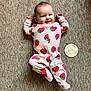 Lily is registered to the contest to win money with this photo: baby, infant, smiling, onesie, strawberry_pattern, carpet, wooden_sign, lying_down, happy, cute, child, face, person, footed_pajamas, indoor, soft_lighting, playful, young, adorable, newborn