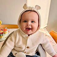 Lily joined the competition — help win amazing prizes! baby, child, smiling, hoodie, knitted, white, blue_eyes, cute, happy, indoor, table, chair, toy, buttoned_clothing, portrait, seated, infant, face, warm_clothing, playful