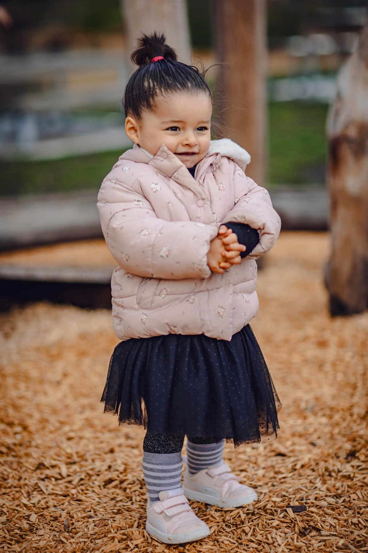 Giulia participe au concours pour gagner de l'argent avec cette photo : child, puffy_jacket, black_skirt, striped_socks, white_shoes, wood_chips, playground, outdoor, smile, standing, pony_tail, cute, winter_clothing, fashion, happy, person, young_child, casual, nature, park