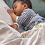 toddler, sleeping, bed, pillow, blanket, pacifier, striped_shirt, curly_hair, child, indoor, cozy, resting, soft, floral, white_bedding, green_pillow, cute, peaceful, person, nap