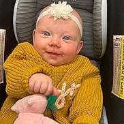 Braelynn is registered to the contest to win money with this photo: baby, child, car_seat, knitted_sweater, yellow_sweater, headband, flower_headband, plush_toy, pink_toy, pacifier, smiling, happy, cute, infant, clothing, indoor, person, seated, blue_jeans, closeup