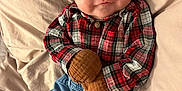 Sylas is registered to the contest to win money with this photo: baby, infant, smile, plaid_shirt, mittens, blue_pants, white_socks, blanket, bed, cute, happy, child, clothing, person, portrait, indoor, cozy, resting, soft, young