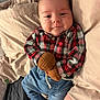 baby, infant, smile, plaid_shirt, mittens, blue_pants, white_socks, blanket, bed, cute, happy, child, clothing, person, portrait, indoor, cozy, resting, soft, young