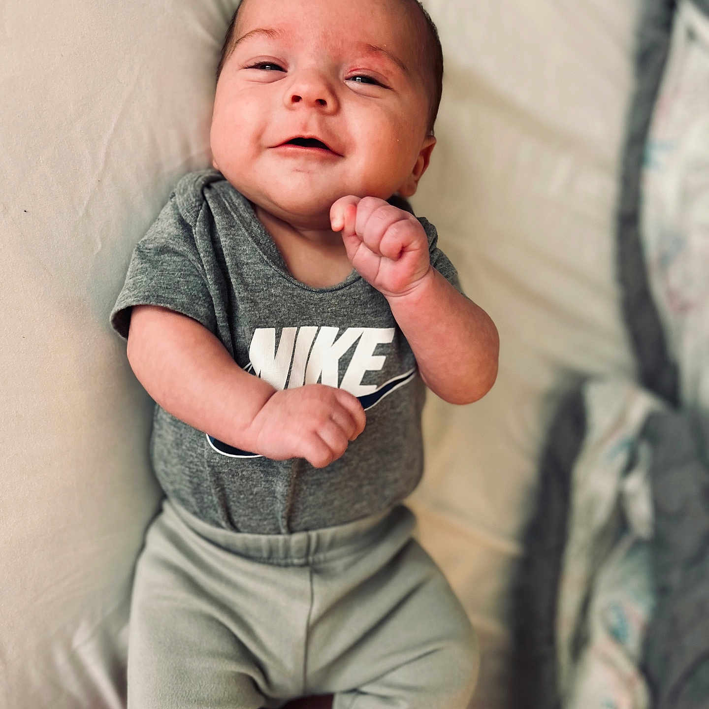 Sylas is registered to the contest to win money with this photo: baby, bed, blanket, casual, child, clothing, comfort, cute, face, hand, happy, infant, lying_down, onesie, pants, person, rest, skin, smile, young