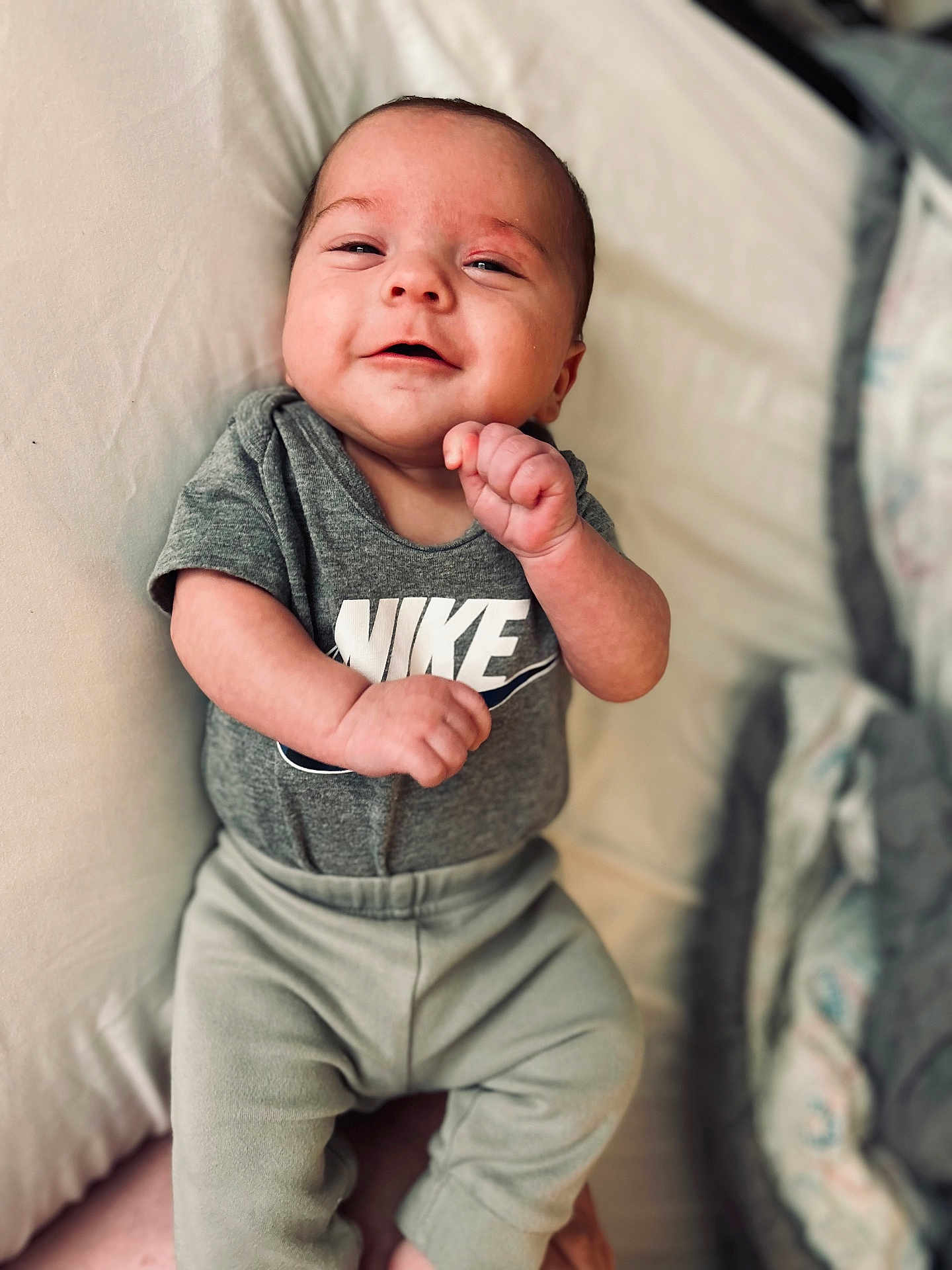 Sylas is registered to the contest to win money with this photo: baby, infant, smile, clothing, onesie, pants, bed, blanket, person, face, happy, cute, child, young, skin, hand, lying_down, rest, comfort, casual