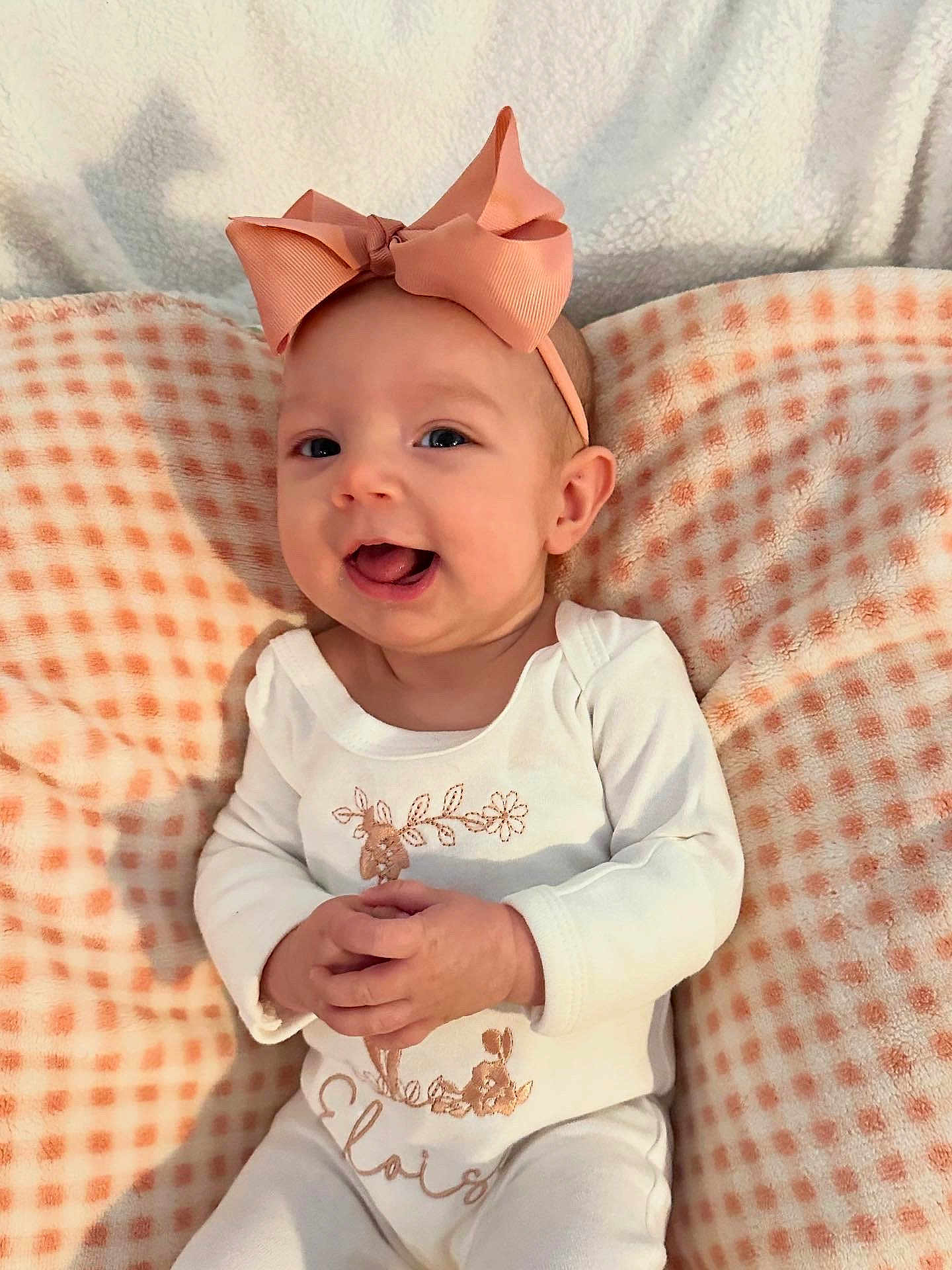 Eloise is registered to the contest to win money with this photo: baby, bow, pink, smiling, cute, infant, white_clothing, blanket, checkered_pattern, soft_texture, happy, portrait, child, indoor, hands, headband, face, sitting, cozy, adorable