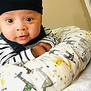 Eithan is registered to the contest to win money with this photo: baby, infant, hat, striped_clothing, pillow, giraffe_pattern, indoor, face, wide_eyes, curious, cute, child, person, bed, blanket, soft_furniture, cozy, portrait, expression, young