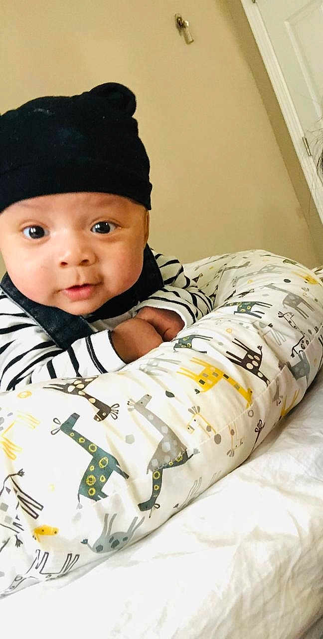 Eithan is registered to the contest to win money with this photo: baby, infant, hat, striped_clothing, pillow, giraffe_pattern, indoor, face, wide_eyes, curious, cute, child, person, bed, blanket, soft_furniture, cozy, portrait, expression, young